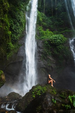 Maceraperest bir kadın bereketli bir ormanda kayalık bir şelaleyi keşfeder..