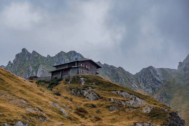 An ancient hotel perched on a cliff high in the Carpathian Mountains, with even taller peaks rising behind it. clipart