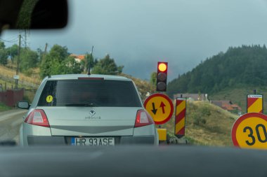 Romanya, Brasov, 09.01.2024 - Kırsal bir yolda trafik işaretleri ve saatte 30 km hız sınırı yakınında kırmızı ışıkta bir araba bekliyor. Sahne, arka planda evler ve ağaçlarla dolu tepelik bir kırsalda geçiyor.