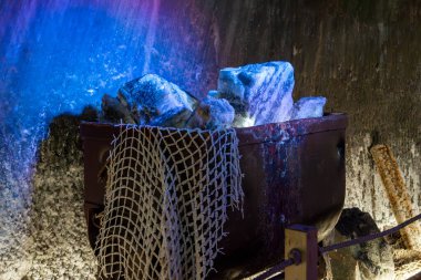 Turda, Romanya, 20 Ekim 2024: Salina Turda 'nın içinde mavi ve mor ışıklarla aydınlatılmış tuz bloklarıyla dolu bir maden arabası, madenlerin sanayi mirası ve jeolojik tarihini vurguluyor.