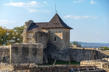 Suceava Kalesi, eğimli bir çatısı olan tarihi bir taş yapı, açık mavi gökyüzüne karşı kurulmuş, mimari önemini vurguluyor..