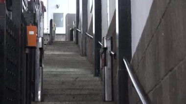 Ulaşım platformuna doğru giden bir merdivenin görüntüsü, içinde güvenli bir turnike kapısı var. Görüntü ulaşım, güvenlik ve kentsel mimari temalarını yansıtıyor.