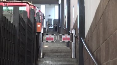 Ulaşım platformuna doğru giden bir merdivenin görüntüsü, içinde güvenli bir turnike kapısı var. Görüntü ulaşım, güvenlik ve kentsel mimari temalarını yansıtıyor.