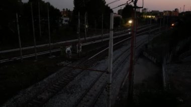 Bir yük treni gece loş bir kentsel ortamda sürekli hareket ederek ulaşım yönünü ve endüstriyel atmosferi vurguluyor..
