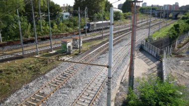 Bir tren, doğa ve kentleşmenin bir karışımını betimleyen, grafiti kaplı yapılar ve yemyeşil ile çevrili kentsel demiryolu rayları boyunca seyahat eder..