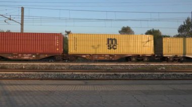 Milan, İtalya, 15 Kasım 2024: Demiryolu üzerinden geçen renkli konteynırlarla dolu yük treni, ulaşım, lojistik ve küresel ticareti simgeliyor. Bu dinamik sahne modern endüstrinin ve hareketin özünü yakalar..