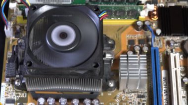 Karmaşık elektronik parçalarla çevrili aktif bir soğutma vantilatörünü gösteren bir bilgisayar anakartının detaylı görüntüsü. Modern bilgisayar cihazlarının arkasındaki karmaşıklığı ve teknolojiyi yakalar.