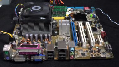 Karmaşık elektronik parçalarla çevrili aktif bir soğutma vantilatörünü gösteren bir bilgisayar anakartının detaylı görüntüsü. Modern bilgisayar cihazlarının arkasındaki karmaşıklığı ve teknolojiyi yakalar.
