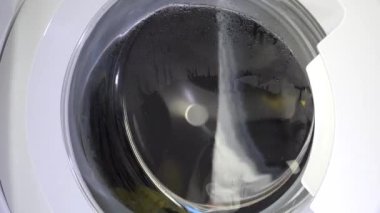 Çağdaş ev aletlerinin dinamik enerjisini yakalayan, şeffaf kapıdan dönen çamaşırları gösteren hareket halindeki bir çamaşır makinesinin yakın çekim görüntüsü..