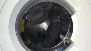 Çağdaş ev aletlerinin dinamik enerjisini yakalayan, şeffaf kapıdan dönen çamaşırları gösteren hareket halindeki bir çamaşır makinesinin yakın çekim görüntüsü..