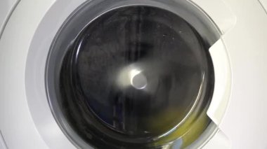 Çağdaş ev aletlerinin dinamik enerjisini yakalayan, şeffaf kapıdan dönen çamaşırları gösteren hareket halindeki bir çamaşır makinesinin yakın çekim görüntüsü..