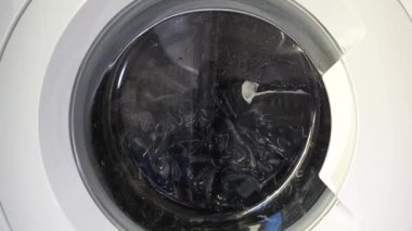 Çağdaş ev aletlerinin dinamik enerjisini yakalayan, şeffaf kapıdan dönen çamaşırları gösteren hareket halindeki bir çamaşır makinesinin yakın çekim görüntüsü..