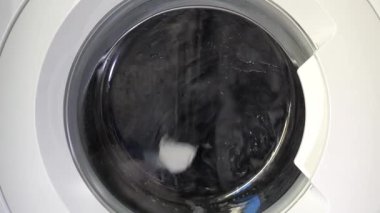 Çağdaş ev aletlerinin dinamik enerjisini yakalayan, şeffaf kapıdan dönen çamaşırları gösteren hareket halindeki bir çamaşır makinesinin yakın çekim görüntüsü..