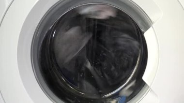 Çağdaş ev aletlerinin dinamik enerjisini yakalayan, şeffaf kapıdan dönen çamaşırları gösteren hareket halindeki bir çamaşır makinesinin yakın çekim görüntüsü..