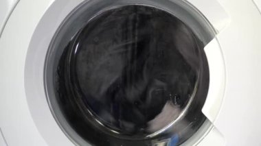 Çağdaş ev aletlerinin dinamik enerjisini yakalayan, şeffaf kapıdan dönen çamaşırları gösteren hareket halindeki bir çamaşır makinesinin yakın çekim görüntüsü..
