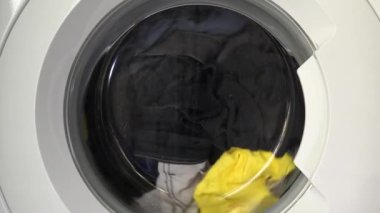 Çağdaş ev aletlerinin dinamik enerjisini yakalayan, şeffaf kapıdan dönen çamaşırları gösteren hareket halindeki bir çamaşır makinesinin yakın çekim görüntüsü..