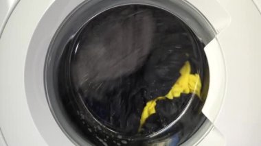 Çağdaş ev aletlerinin dinamik enerjisini yakalayan, şeffaf kapıdan dönen çamaşırları gösteren hareket halindeki bir çamaşır makinesinin yakın çekim görüntüsü..