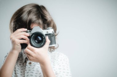 Beyaz gömlekli ve mavi elbiseli bir çocuk antika fotoğraf makinesiyle fotoğraf çekiyor..