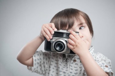 Beyaz gömlekli ve mavi elbiseli bir çocuk antika fotoğraf makinesiyle fotoğraf çekiyor..  