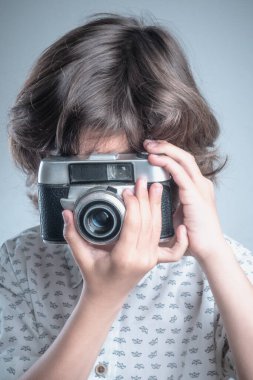 Beyaz gömlekli ve mavi elbiseli bir çocuk antika fotoğraf makinesiyle fotoğraf çekiyor..  