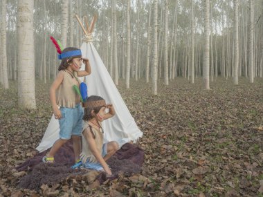 Çadırın yanında Kızılderili rolü yapan ikizler ve elleri kafalarında ufka bakıyorlar.. 