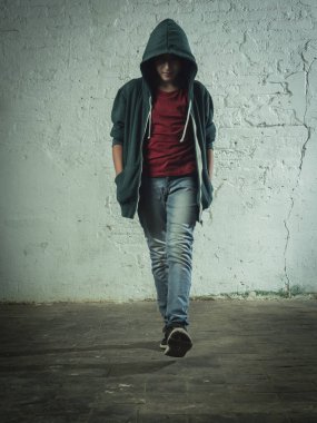 Çocuk kapüşonu açık ve kapüşonlu bir şekilde kameraya doğru yürüyor. Kentsel ve endüstriyel çevre.