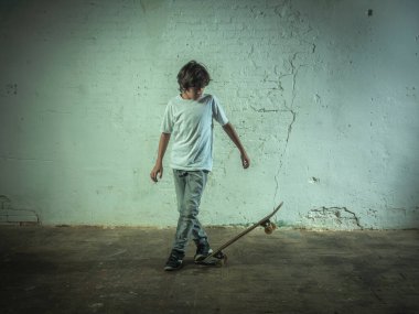 Beyaz bir duvarın önünde kaykay yapan bir çocuk..