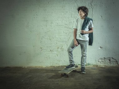 Omzunda kazağı ve kaykayıyla ayakta duran bir çocuğun portresi.. -