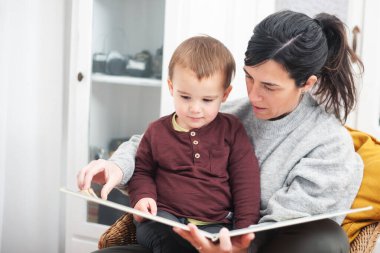 Anne içeride hasır bir sandalyede oğluna kitap okuyor..