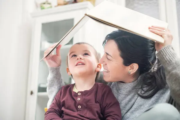 Anne kendini ve çocuğunu sanki bir evin çatısındaymış gibi bir kitapla kaplıyor, kitapta geçen hikayeyi göstermek için..