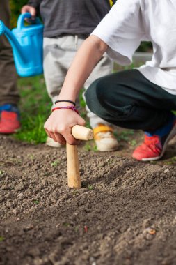 Bahçedeki bir toprak parçasında ahşap saplı matkap kullanan çocuk kardeşleriyle ilgileniyor.. 