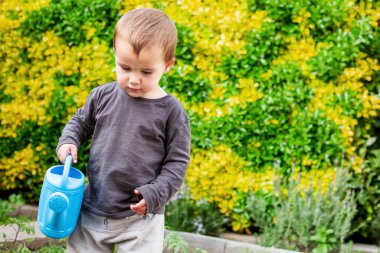 Çocuk elinde mavi bir su bidonuyla yürüyor ve sebze bahçesini suluyor.. 