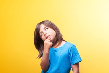 Kahverengi saçlı bir çocuk elini üzerine koyup dalgın bir poz verir. 