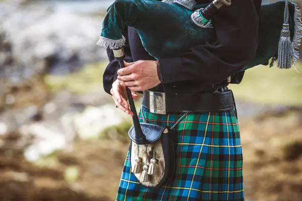 A man wearing a kilt and holding a pipe. The man is dressed in traditional Scottish clothing and is playing a pipe. Concept of cultural pride and heritage, as well as a connection to the past