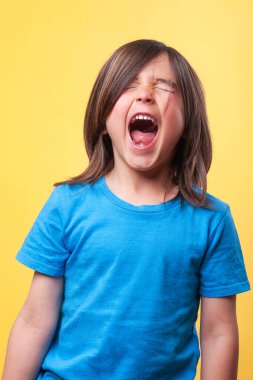 Çığlık atan çocuğa yakın çekim. Mavi tişört giyiyordu. Sarı arka plan. Duygular