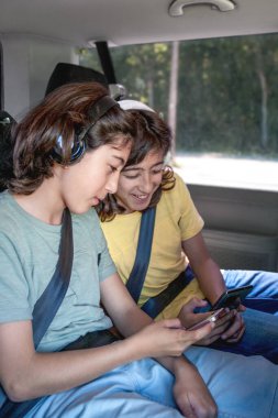 Kulaklıklı ikiz kardeşler minibüste otururken cep telefonlarına bakarlar. 