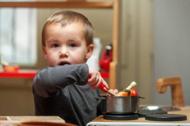Çocuk yemek pişirmek için metal tencereye ahşap yemek karıştırıyor. Sembolik oyun. 