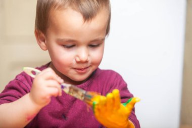 Çocuk elini fırça ve boyayla boyuyor. Oyuncu etkinliği. 