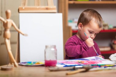 Evdeki oyun odasında resim yapan çocuk. Arkasında tuval olan bir sehpa.. 