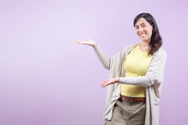 Kadın gülümsüyor ve açık mor arka planda reklam metni için mekan sunuyor. Sahne neşeli ve pozitif..