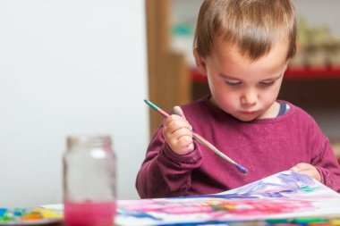 Çocuk evde bir sanat etkinliği sırasında boya fırçasıyla resim yaparken konsantre oluyor.. 