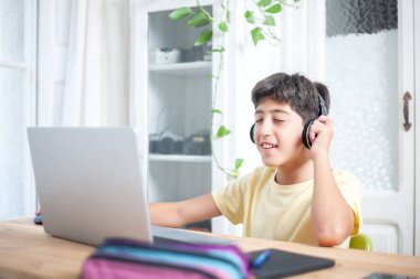 Genç öğrenci, evindeki masasında laptopuyla çalışırken kulaklıkla müzik dinleyerek rahatlıyor.. 