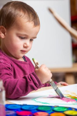 Küçük bir çocuk boya fırçasıyla boş bir kağıt parçasına resim çiziyor.. 