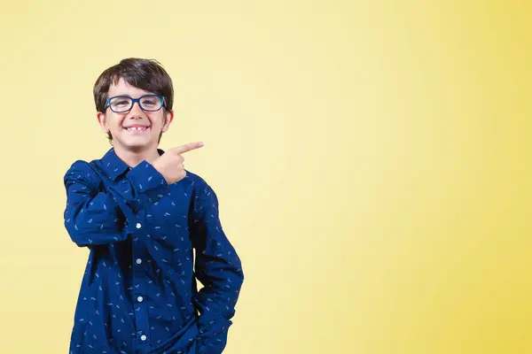 Gülümseyen çocuk sarı arka planda dururken pazarlama için kopyalama alanını işaret ediyor.