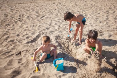 Üç çocuk kumsalda kumsalda oynuyorlar. Sahne neşeli ve kaygısız..