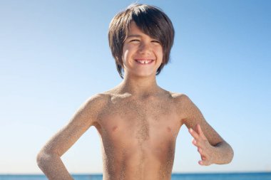 Çocuk gülümseyen kameraya bakıyor kumsaldan gelen kumlarla dolu vücuduyla.. 