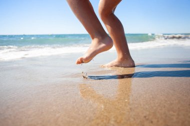 Tanınmayan bir çocuğun ayakları sahilde koşuyor. Ayakları suyun içinde.. 