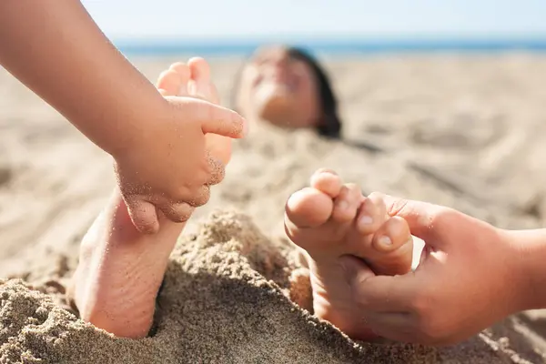 Bir çocuğun ayaklarına yakın çekim gülüyor. Kardeşleri onu gıdıklarken sahilde gömülüyordu.