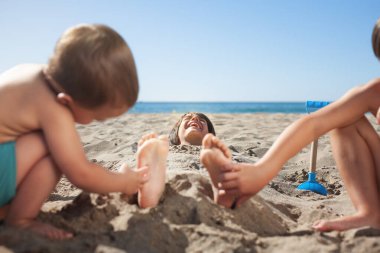 Kumsalda kumlara gömülü bir çocuk kardeşleri ayaklarını gıdıkladığında güler.. 