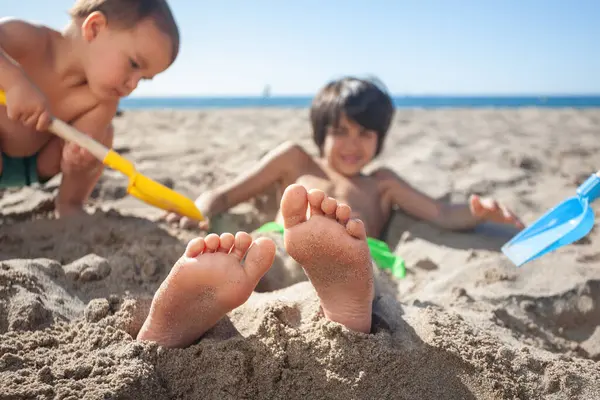 Kardeşleri tarafından kumsalda toprağa gömülen bir çocuğun ayaklarına yakın çekim.. 